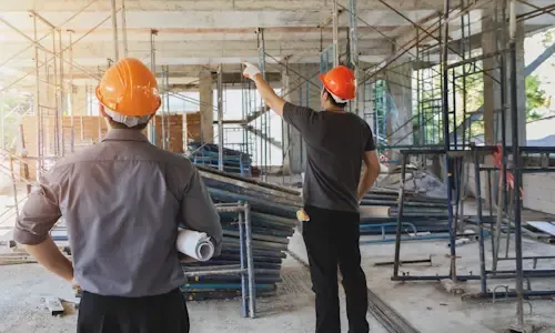 Twee mannen met oranje bouwhelm bespreken een project in een pand in aanbouw