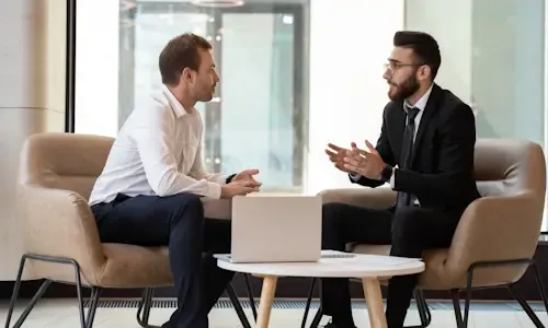 Twee zakelijk geklede mannen in overleg aan een tafel met een laptop